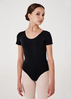 Young dancer wearing black cap sleeve leotard standing in studio setting.
