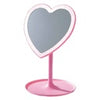 A pink vanity mirror with a heart-shaped reflective surface and a round pink stand, shown against a plain white background.