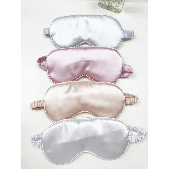 Assorted Love and Repeat satin eye masks stacked in soft neutral and pastel colors