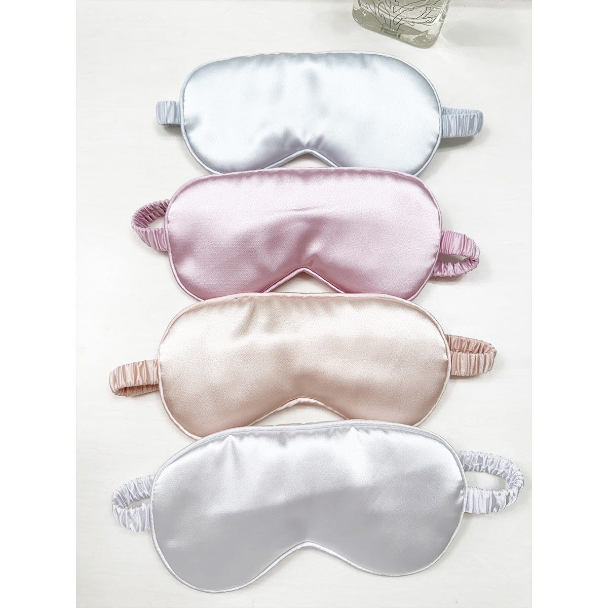 Assorted Love and Repeat satin eye masks stacked in soft neutral and pastel colors