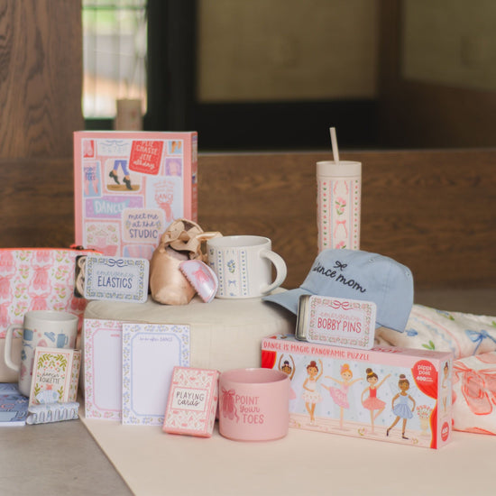 Collection of pink-themed products including mugs, books, and a candle on a wooden surface.