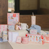 Collection of pink-themed products including mugs, books, and a candle on a wooden surface.