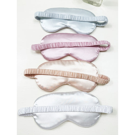 Love and Repeat satin sleeping masks arranged in assorted pink, white, champagne, and grey tones