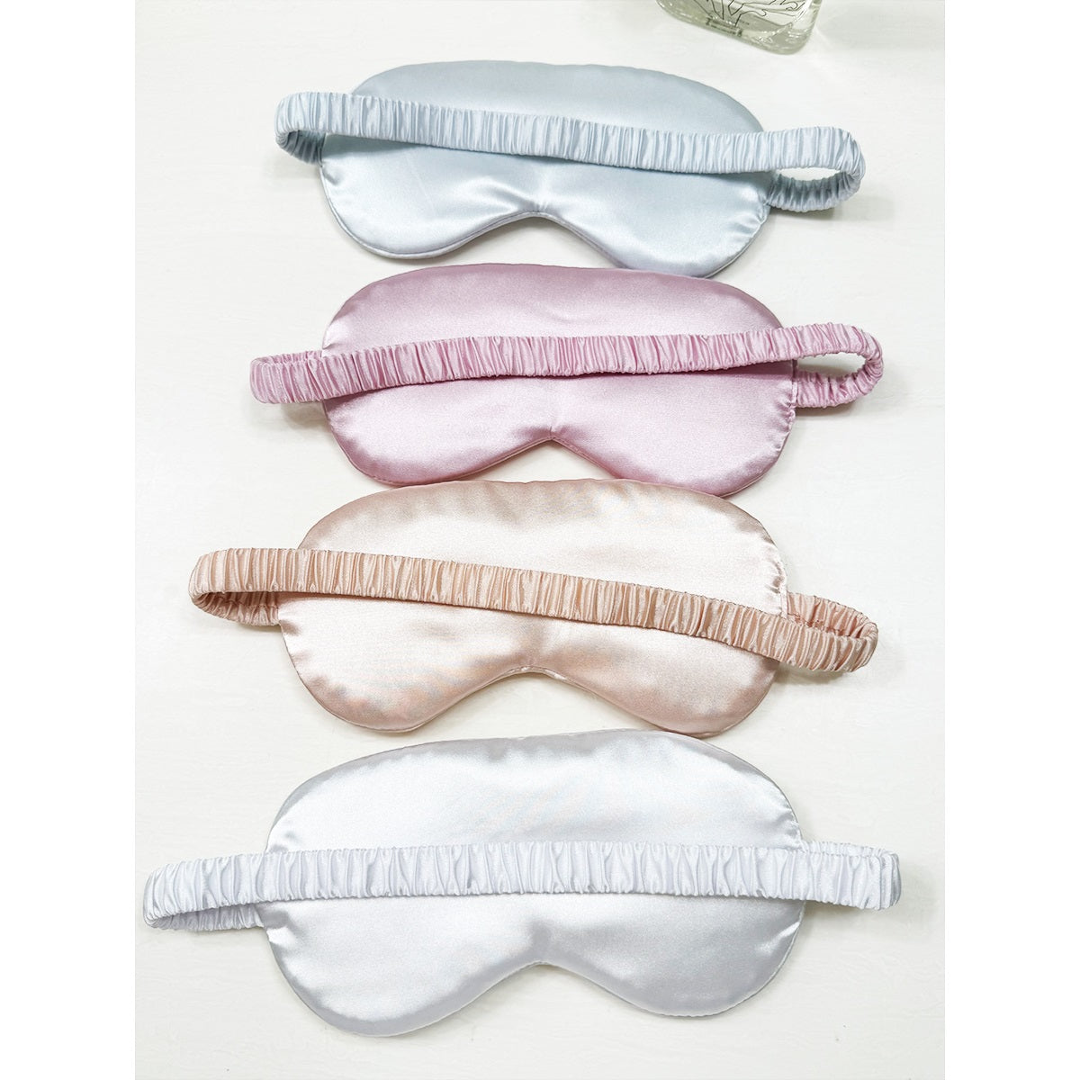 Love and Repeat satin sleeping masks arranged in assorted pink, white, champagne, and grey tones