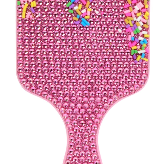 A pink hairbrush covered in rhinestones, with a handle and paddle head decorated with colorful sprinkle-like embellishments on a white background.