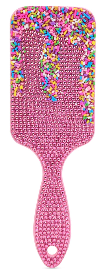 A pink hairbrush covered in rhinestones, with a handle and paddle head decorated with colorful sprinkle-like embellishments on a white background.