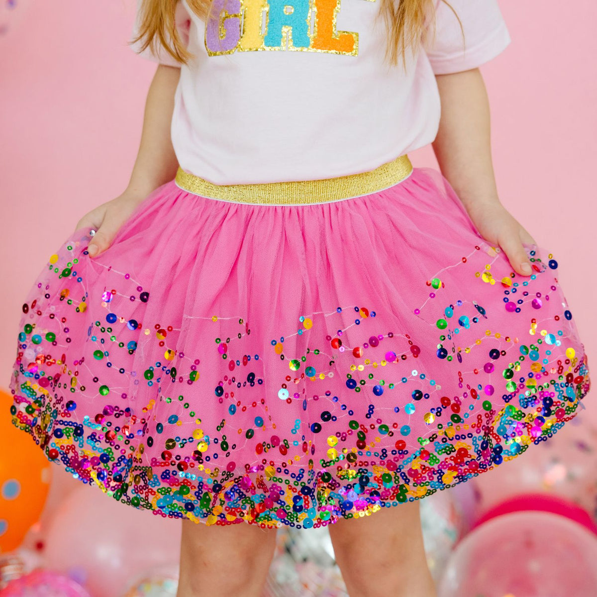 Close-up of raspberry pink tutu skirt showing colorful sequin embellishments and gold waistband