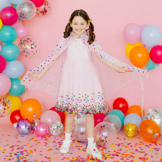 Young girl modeling pink confetti cape with balloons and party decorations