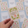 A hand holds a small illustrated card deck box labeled "dancer roulette" against a light blue background with matching cards scattered around.