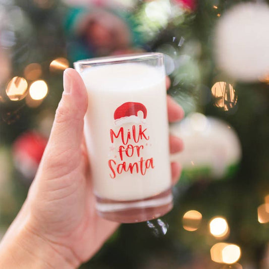 Hand holding a mini milk for Santa glass in front of Christmas decor