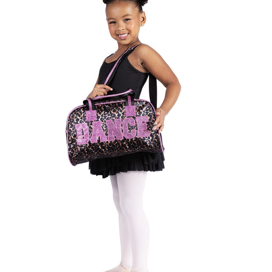 Young dancer holding black animal print dance duffle bag with pink “DANCE” lettering