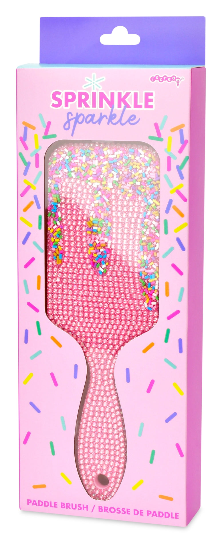 Pink rhinestone-embellished paddle brush in its retail packaging, featuring a pink handle and a clear window showing the sparkly bristles. The box has a purple header and colorful sprinkle graphics.