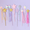 A set of nine pastel-themed toy or costume wands with star, bow, snowflake, and tassel designs, arranged on a light lavender background.