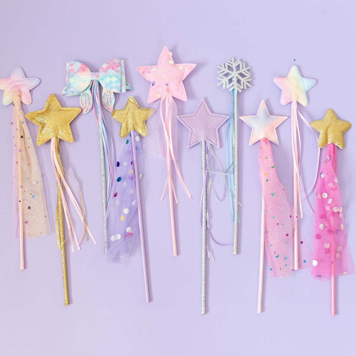 A set of nine pastel-themed toy or costume wands with star, bow, snowflake, and tassel designs, arranged on a light lavender background.