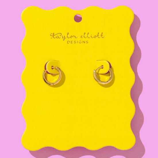 Gold huggie earrings displayed on a bright yellow scalloped backer card with Taylor Elliot Designs branding.