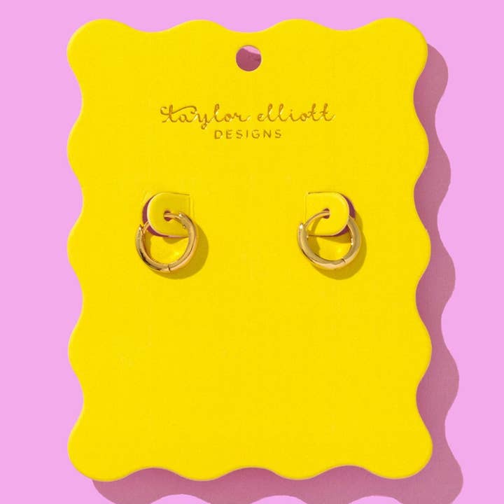 Gold huggie earrings displayed on a bright yellow scalloped backer card with Taylor Elliot Designs branding.