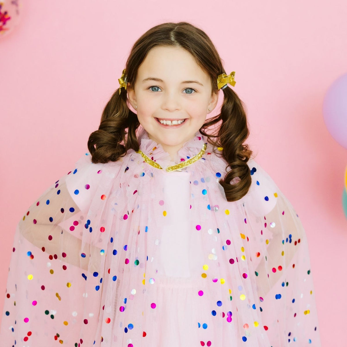Young girl modeling pink confetti cape with multicolor embellishments