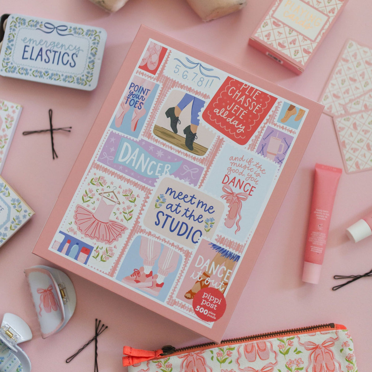A pink gift box with dance-themed illustrations and text, surrounded by matching pink beauty and stationery items on a light pink background.