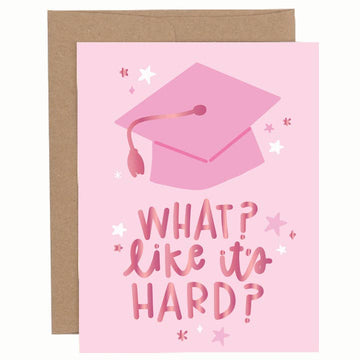 Graduation greeting card with a pink graduation cap illustration and the phrase “What? Like it’s hard?” on a light pink background, shown with a brown envelope.