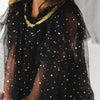 A close-up of a black sheer tulle top or cape decorated with scattered gold stars, moons, and dots, worn by a model.