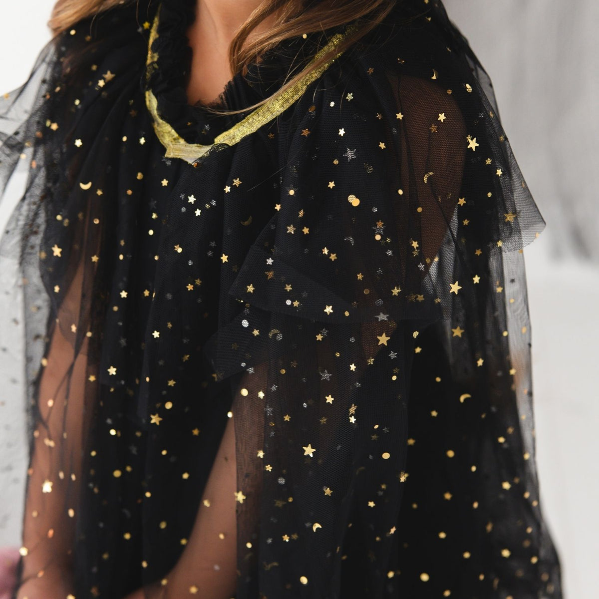 A close-up of a black sheer tulle top or cape decorated with scattered gold stars, moons, and dots, worn by a model.