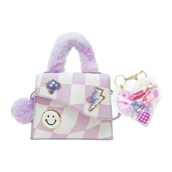 A small lavender and white checkered handbag with fuzzy purple handles, decorative patches including a smiley face and lightning bolt, and a clear heart-shaped keychain filled with colorful charms, shown on a white background.