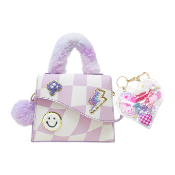 A small lavender and white checkered handbag with fuzzy purple handles, decorative patches including a smiley face and lightning bolt, and a clear heart-shaped keychain filled with colorful charms, shown on a white background.