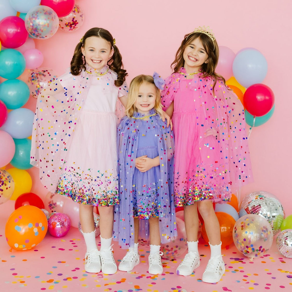 Two girls wearing pink and pastel dress-up capes with colorful confetti details