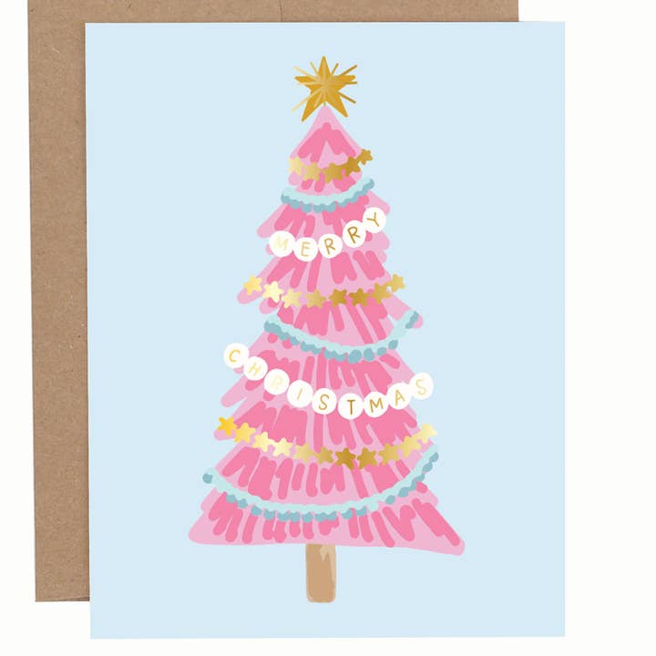 Greeting card with a pink Christmas tree illustrated with bracelet-style garlands and gold star topper on a light blue background, shown with a brown envelope.