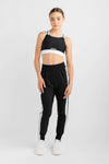 Female dancer wearing black jogger-style dance pants with white side stripes, standing facing forward in a studio pose.