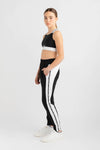 Female dancer wearing black jogger-style dance pants with white side stripes and a black crop top, standing against a light background.