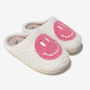 Pair of cream-colored fuzzy slippers with pink smiley faces on the top