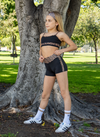 Young dancer wearing black cheetah-print dance shorts and matching top posing outdoors.