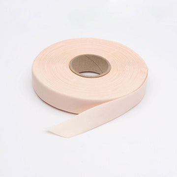 Roll of pale pink satin pointe shoe ribbon with a loose ribbon end on a white background.