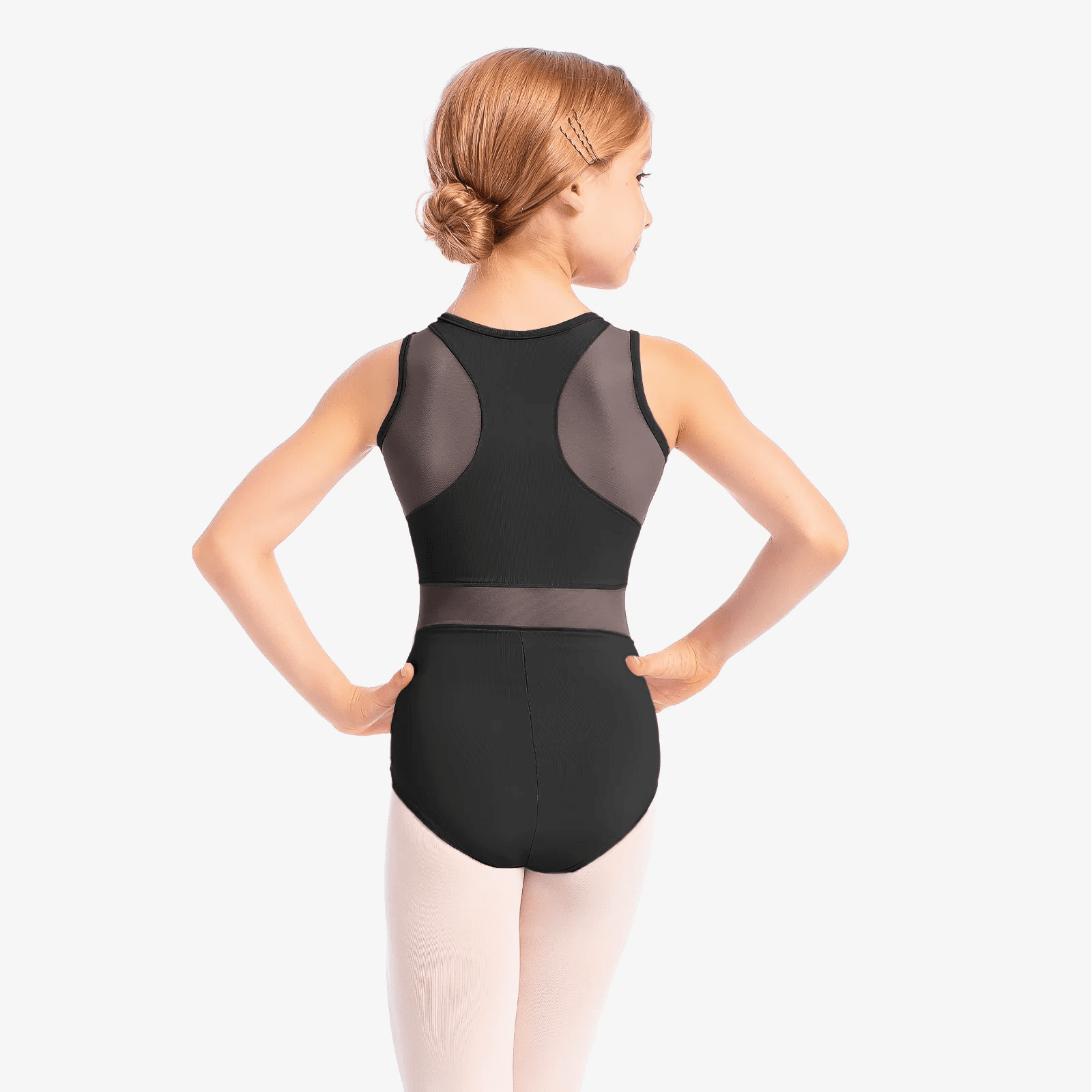 Young dancer wearing black tank leotard with mesh insert while posing in studio