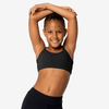 Young dancer wearing a black cropped dance top, posing with arms raised against a light background.