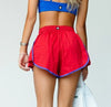 Red pleated dance shorts shown worn on a dancer from the side
