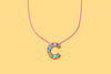 Colorful confetti letter necklace displayed on a pastel backdrop.