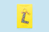 Confetti letter L acrylic keychain on a yellow backer card with gold keyring