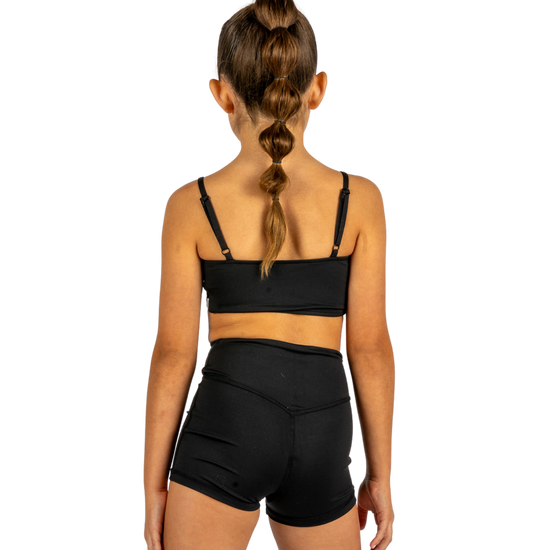 Young dancer wearing black V-waist dance shorts with coordinating top, standing facing forward.