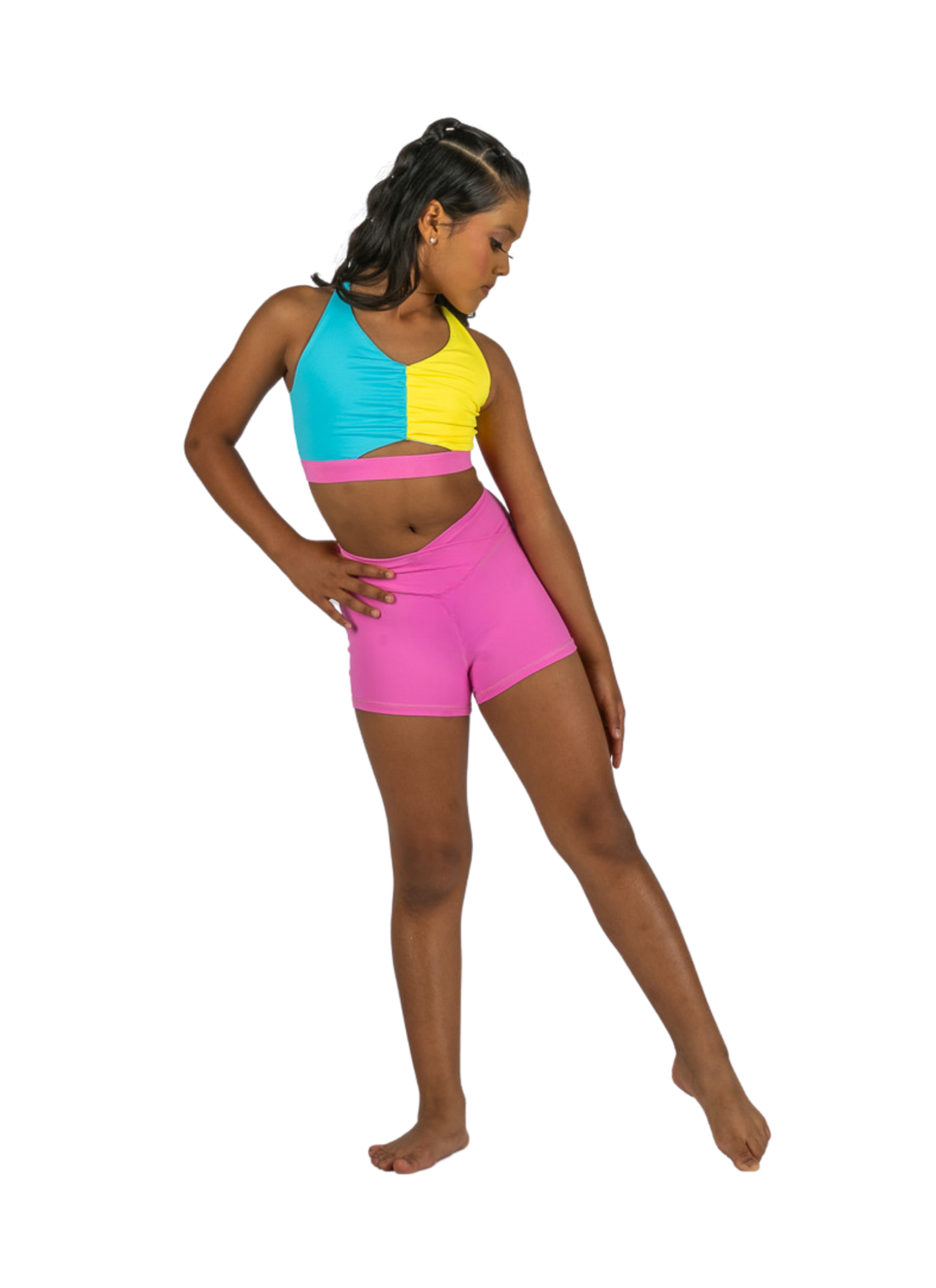 Young dancer wearing pink V-waist dance shorts with a colorful crop top, standing in a studio pose.