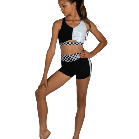 Young dancer wearing a black and white dance top and matching shorts, standing in a confident studio pose.