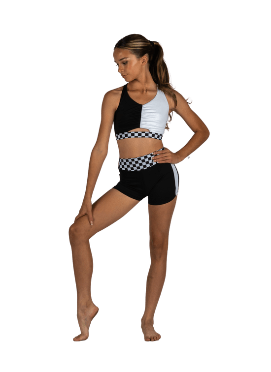 Young dancer wearing a black and white dance top and matching shorts, standing in a confident studio pose.