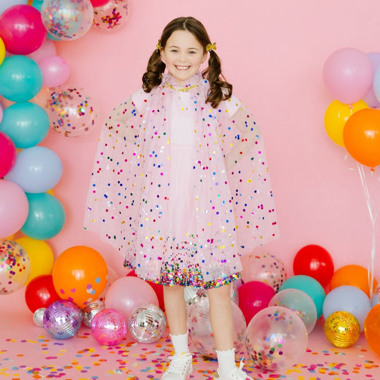 Young girl wearing pink confetti dress-up cape with colorful party decorations