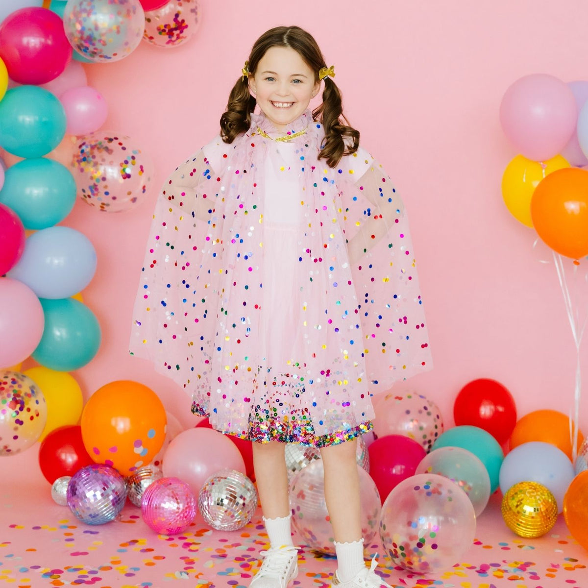 Young girl wearing pink confetti dress-up cape with colorful party decorations