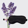 Black weighted satin eye mask displayed next to fresh lavender stems
