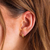 Close-up of a gold huggie earring worn on an ear.