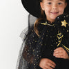 A young girl wearing a black witch costume with gold star details, a black hat, and holding a wand, photographed against a plain white studio background.