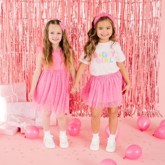 Two girls wearing coordinating pink birthday outfits with colorful party decorations