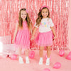 Two girls wearing coordinating pink birthday outfits with colorful party decorations